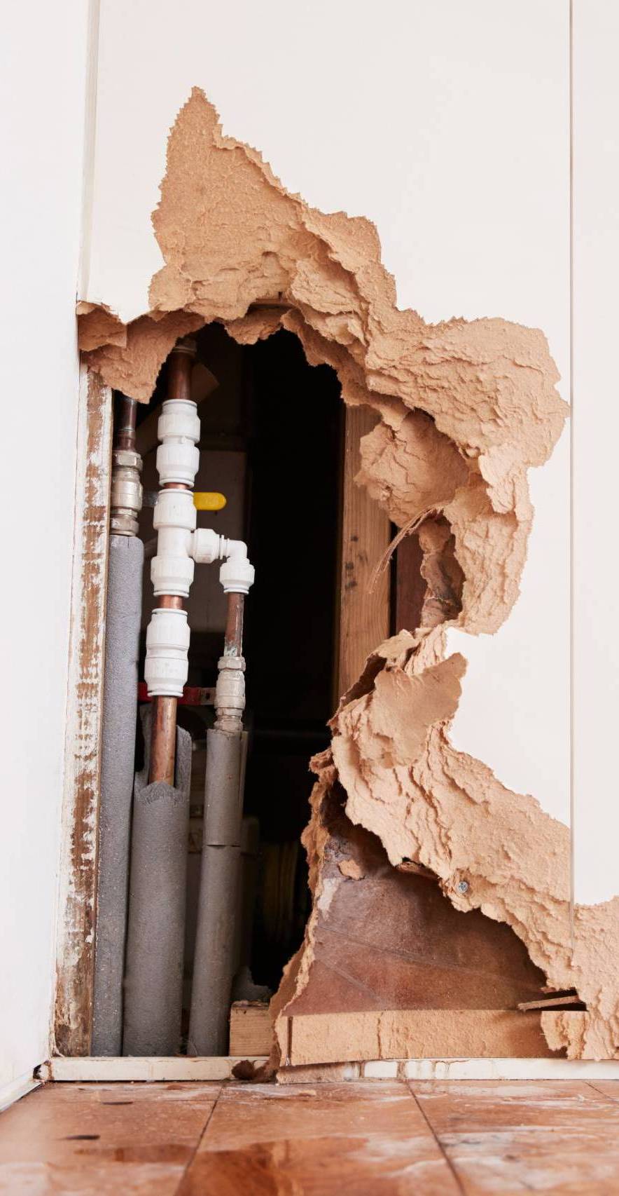 Damaged wall exposing burst water pipes after flood